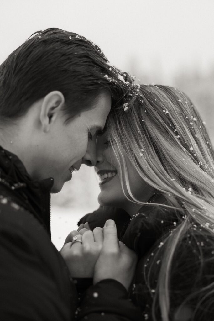 Engagement ring pictured with couple nose to nose as snow falls on them.